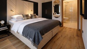 A modern bedroom with a large bed, bedside tables, a mirror, and a walk-in shower. - Wonderful ski in-ski out chalet with Sauna (Sankt Lambrecht)