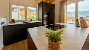 A modern kitchen with a central island, black cabinetry, and a view of a residential area through large windows. - Wonderful ski in-ski out chalet with Sauna (Sankt Lambrecht)