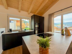 A modern kitchen with a central island, black cabinetry, and a view of a residential area through large windows. - Wonderful ski in-ski out chalet with Sauna (Sankt Lambrecht)