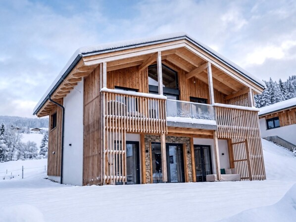 Eine Holzhütte mit Balkon, Steinaußenwand und verschneiter Landschaft.