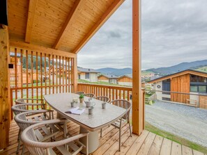 Eine Holzterrasse mit Tisch und Stühlen, mit Blick auf eine ländliche Landschaft mit Häusern und Bergen.