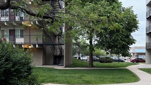 Un edificio de varios pisos con una escalera central, rodeado de vegetación y un sendero pavimentado.
