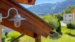 Una estructura de madera con un accesorio de luz metálico y una bandeja, frente a un paisaje de montañas y un edificio.