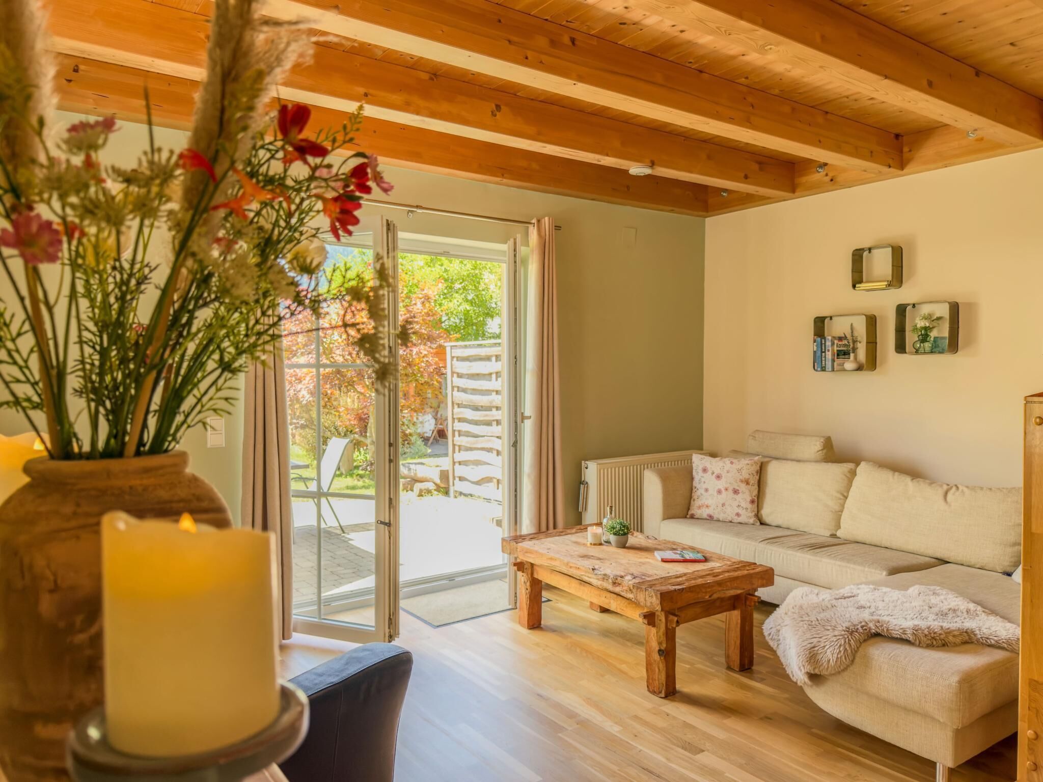 Ein gemütliches Wohnzimmer mit Holzbalkendecke, einer Couch, einem Couchtisch und einer Vase mit Blumen.