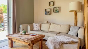 Una sala de estar acogedora con una mesa de centro de madera, un sofá con cojines, una lámpara de pie y una ventana con cortinas.