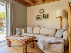 A cozy living room with a wooden coffee table, a sofa with cushions, a floor lamp, and a window with curtains. - Chalet with nice garden and wood-fired hot tub (Kötschach-Mauthen)