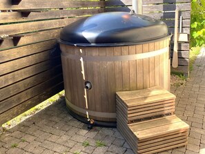A wooden outdoor structure with a metal top, possibly a barbecue or storage unit, next to a wooden bench and a stack of wooden planks. - Chalet with nice garden and wood-fired hot tub (Kötschach-Mauthen)