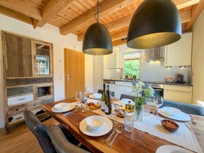 A dining area with a wooden table set for a meal, a kitchen in the background, and a wooden ceiling. - Chalet with nice garden and wood-fired hot tub (Kötschach-Mauthen)