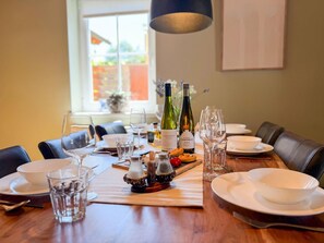 Mesa de comedor dispuesta con botellas de vino, copas y platos, con vistas al exterior a través de una ventana.