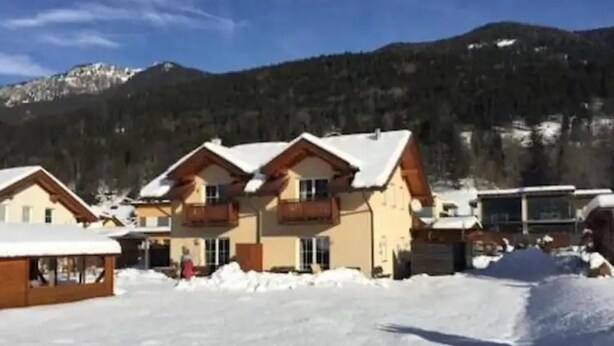 Un complejo turístico en la montaña cubierto de nieve con edificios de estilo chalete, una pista de esquí y cielo despejado.