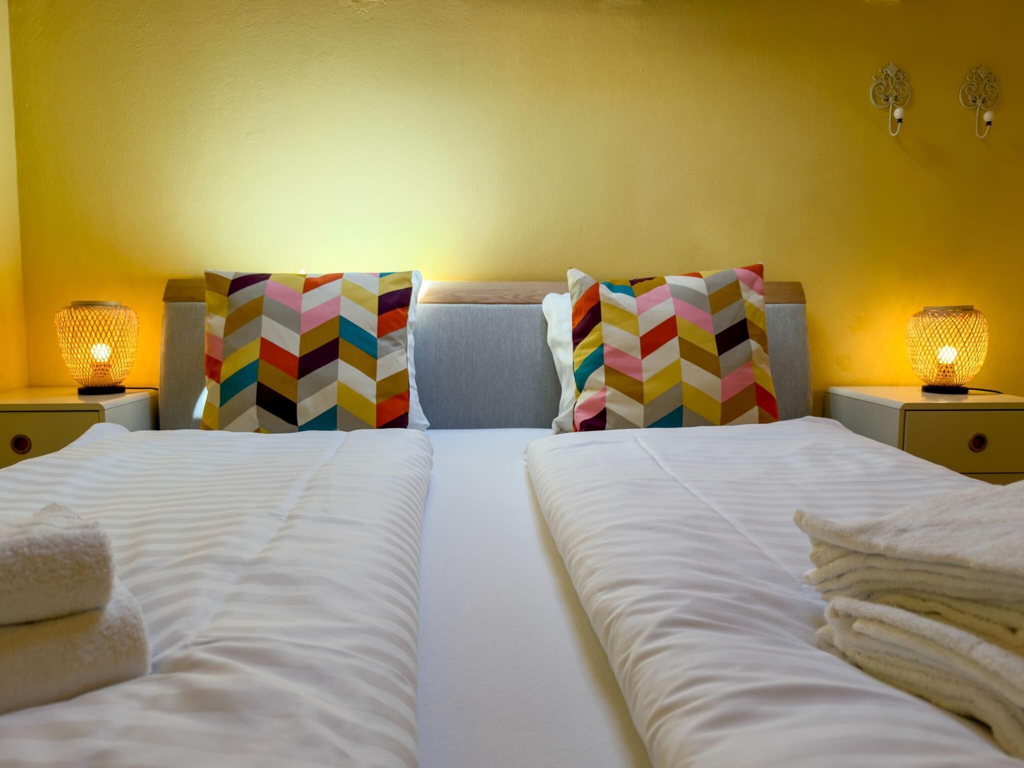 A hotel room with two beds, a nightstand with a lamp, and a wall with two decorative wall sconces.