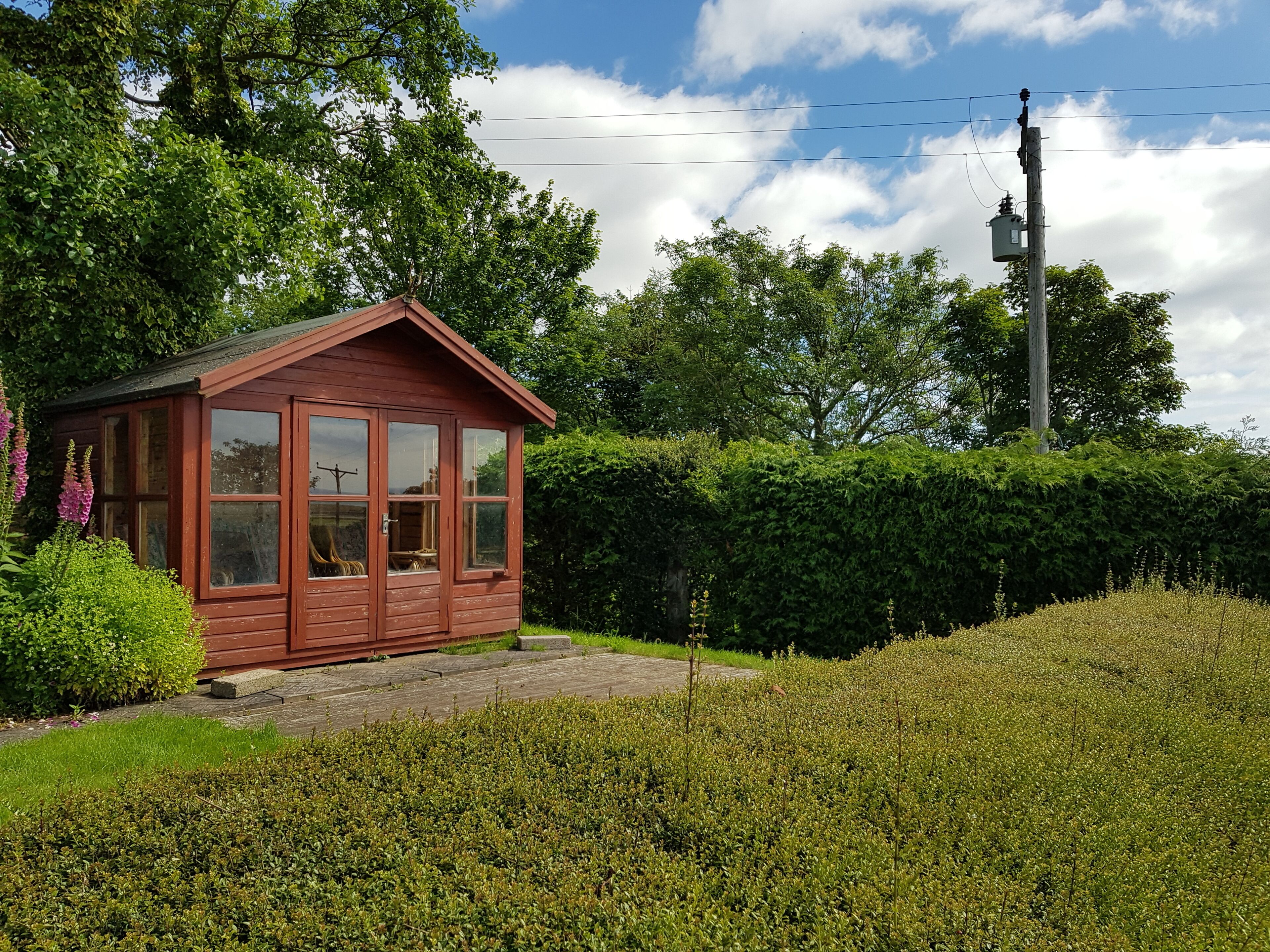 A small wooden cabin with a red roof, large windows, and a stone pathway leading to it.