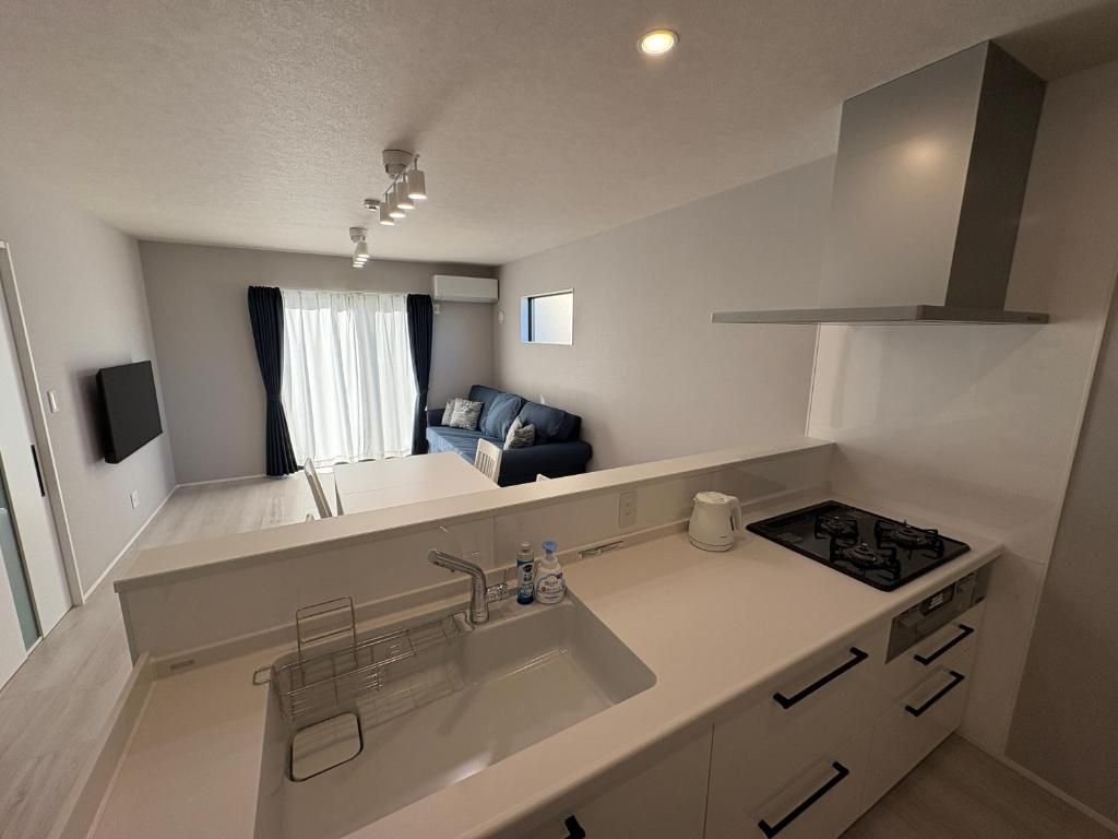 A modern kitchen with a sink, stove, and cabinets, a dining area with a table and chairs, and a living room with a sofa and curtains.
