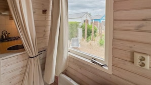 Un interno in legno con una finestra, tende, un termosifone e un angolo cottura con un bollitore.
