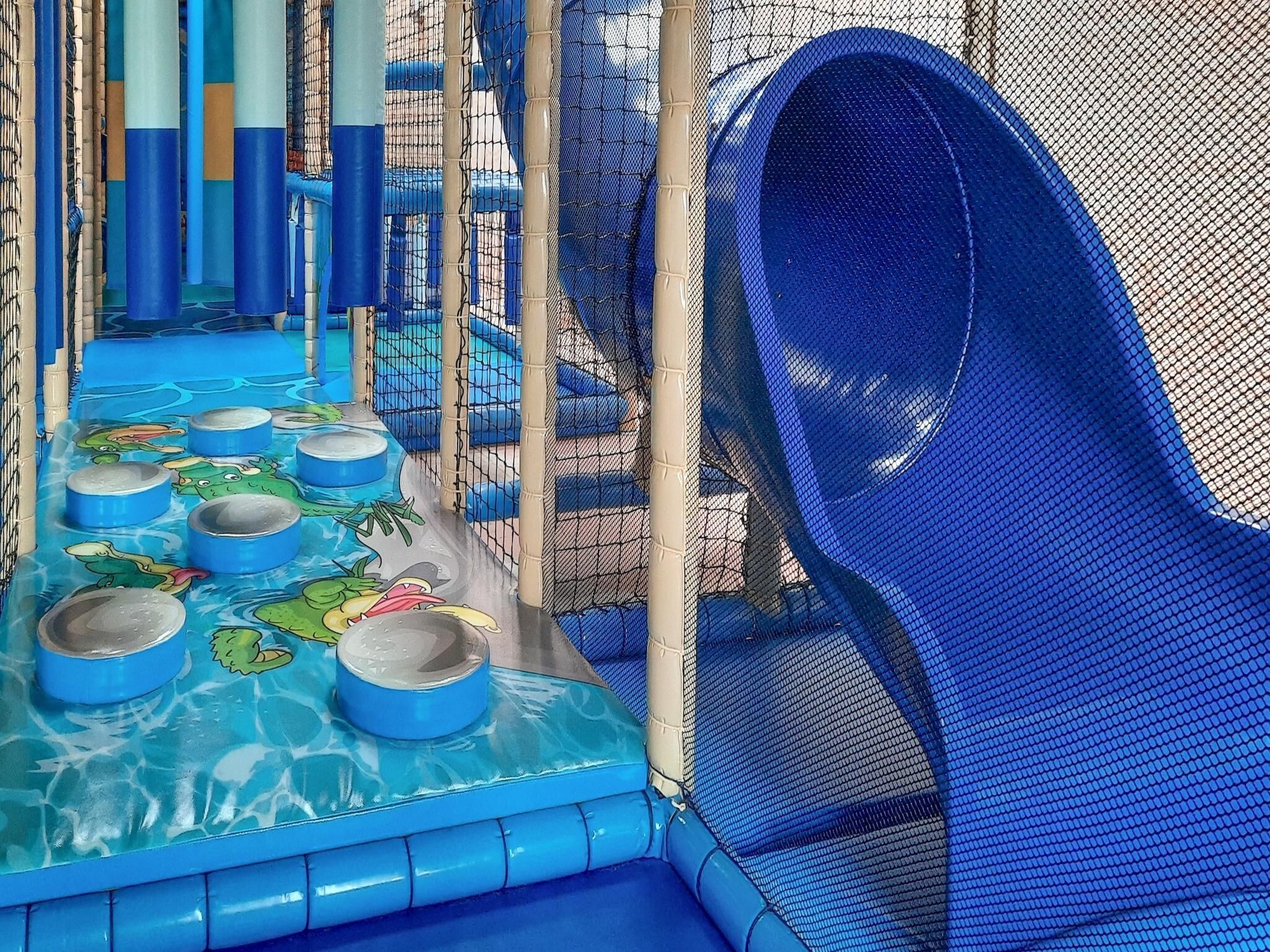 Ein Kinderspielbereich mit einer blauen Rutsche, einem Pool mit Tierfiguren und einer Umzäunung aus Netz.