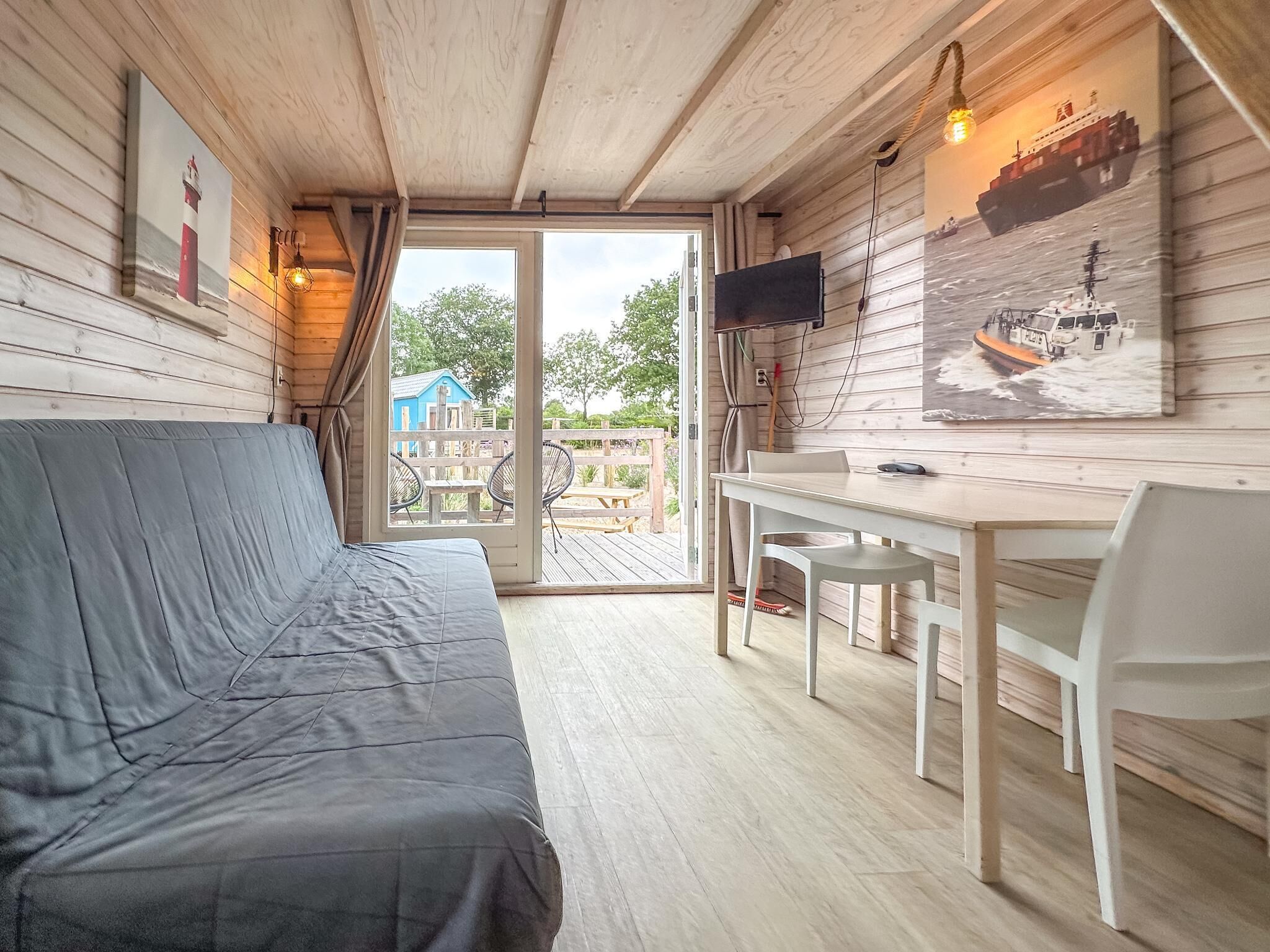 A cabin with a sofa, a table, chairs, a TV, and nautical-themed artwork.