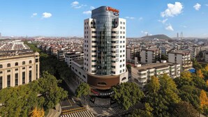 Un hotel de gran altura con una parte superior curva distintiva, rodeado por un paisaje urbano con varios edificios y un cielo despejado.