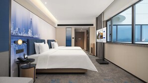 Habitación de hotel con una cama grande, mesitas de noche, un escritorio, una silla, una ventana con vistas a la ciudad y un televisor montado en la pared.