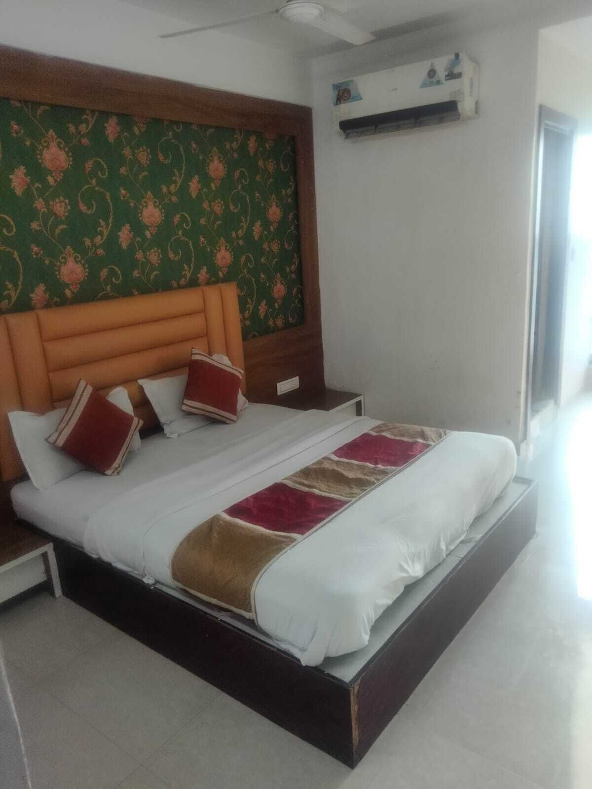 Habitación de hotel moderna con una cama grande, cabecera de madera, pared con diseño verde y un equipo de aire acondicionado.