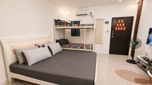 A bedroom with a bed, a bunk bed, a desk, a chair, a fan, and a door with decorations.