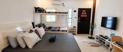 A modern bedroom with a bunk bed, a desk with a computer, a TV, and a door with decorations.