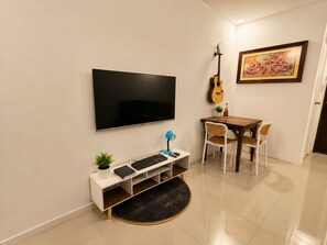 A modern living room with a flat-screen TV, a guitar, a dining table with chairs, and a small plant on a white console table. - Harmony Villa (Tanza)