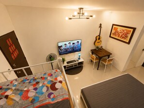 A room with a bed, a desk with a computer, a guitar, a TV, and a door with decorative panels. - Harmony Villa (Tanza)