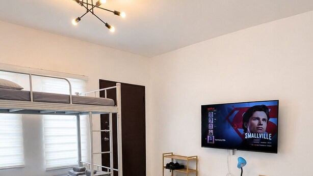 A modern bedroom with bunk beds, a flat-screen TV, a desk, and a bed with a quilted mattress.
