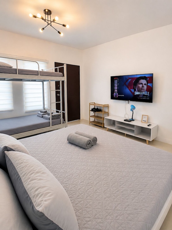 A modern bedroom with bunk beds, a flat-screen TV, a desk, and a bed with a quilted mattress.