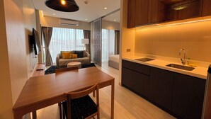 A modern kitchen with a built-in oven, a dining area with a wooden table and chairs, and a living area with a sofa and a TV. - Laguna Lakeside Residences Phuket -YSLL (Tambon Si Sunthon)