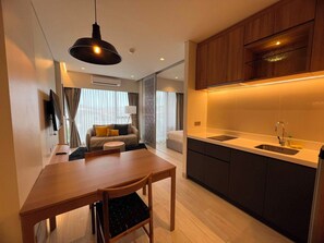 A modern kitchen with a built-in oven, a dining area with a wooden table and chairs, and a living area with a sofa and a TV. - Laguna Lakeside Residences Phuket -YSLL (Tambon Si Sunthon)