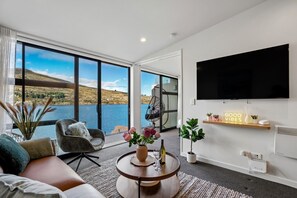 Ein modernes Wohnzimmer mit einem großen Fenster, einem Sofa, einem Couchtisch, einem Fernseher und einem Regal mit Dekoration.