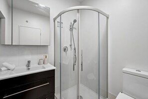 A modern bathroom with a glass-enclosed shower, a white sink with a mirror above, and a black vanity with drawers. - Yooyen Lakeview | 1 BDRM | Luxury | Views (Queenstown)