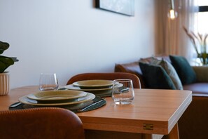 A dining table with plates, glasses, and a fork. There is a chair in front of the table, and a couch in the background. - Yooyen Lakeview | 1 BDRM | Luxury | Views (Queenstown)