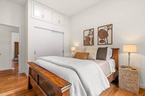 Ein Schlafzimmer mit einem hölzernen Bett, weißen Wänden und zwei gerahmten Pflanzenmotiven.