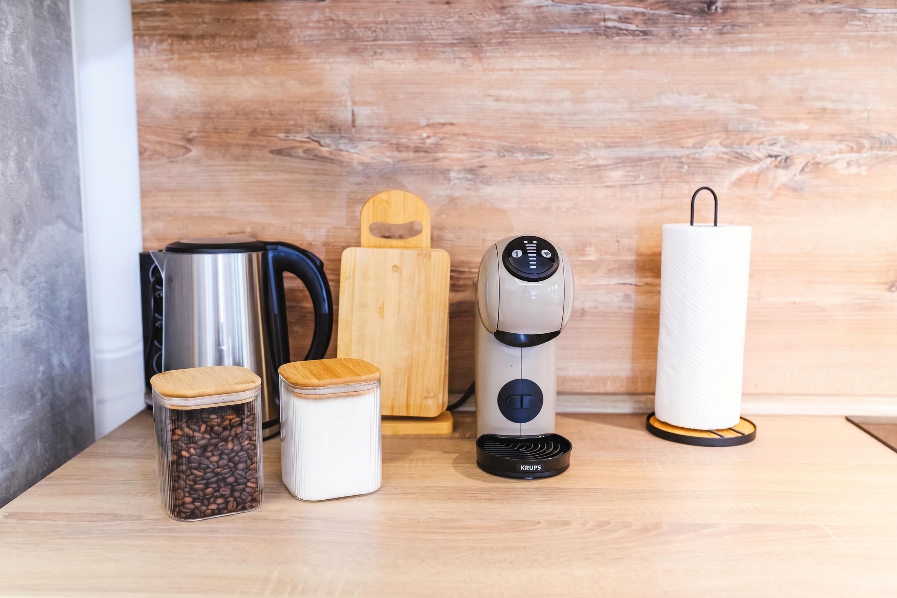 Eine Küchenarbeitsplatte mit Kaffeemaschine, Wasserkocher, Schneidebrett, Kaffeebohnenglas und Küchenpapierrolle.
