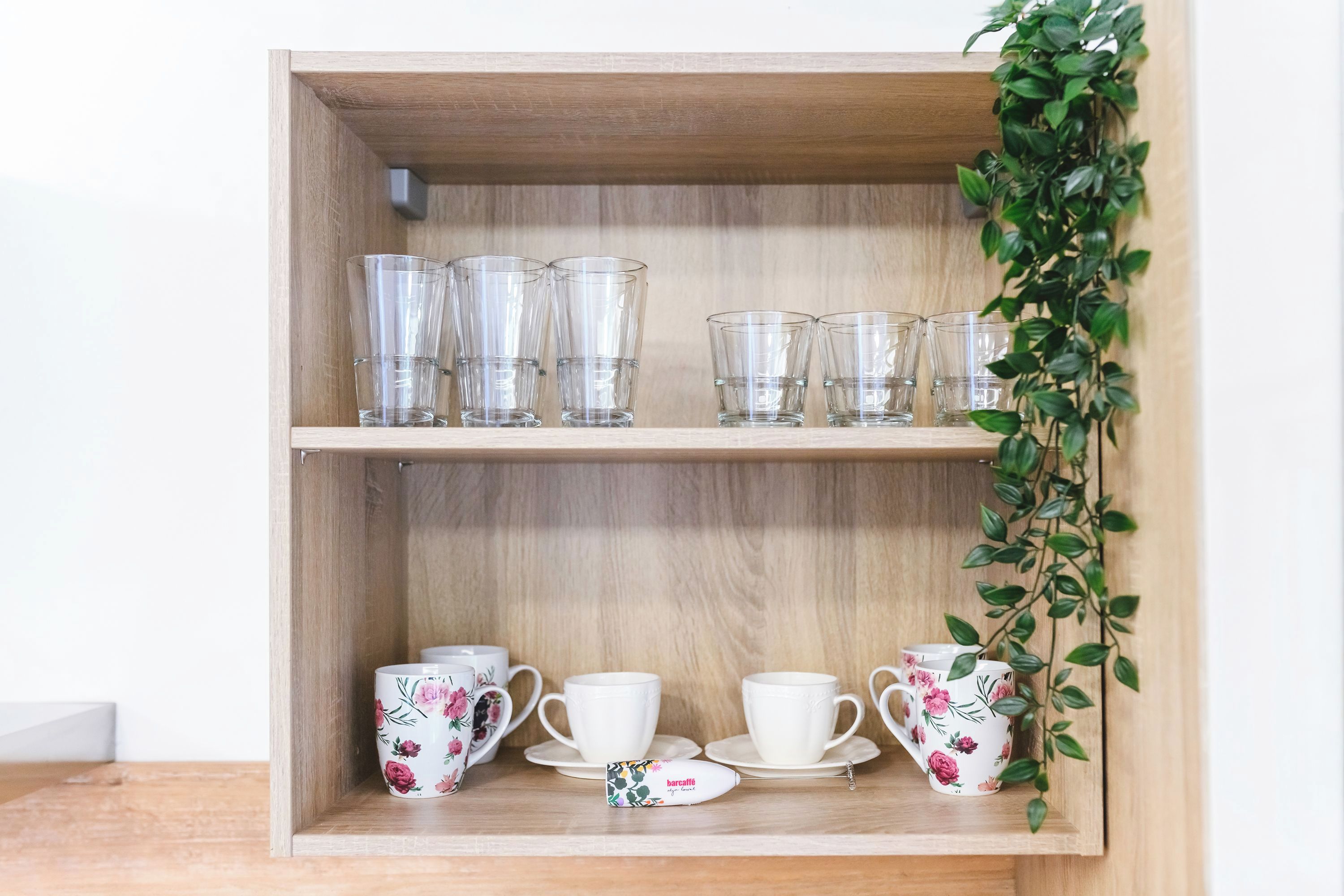 En træhylde med klare drikkeglas og kopper med blomstermønster.