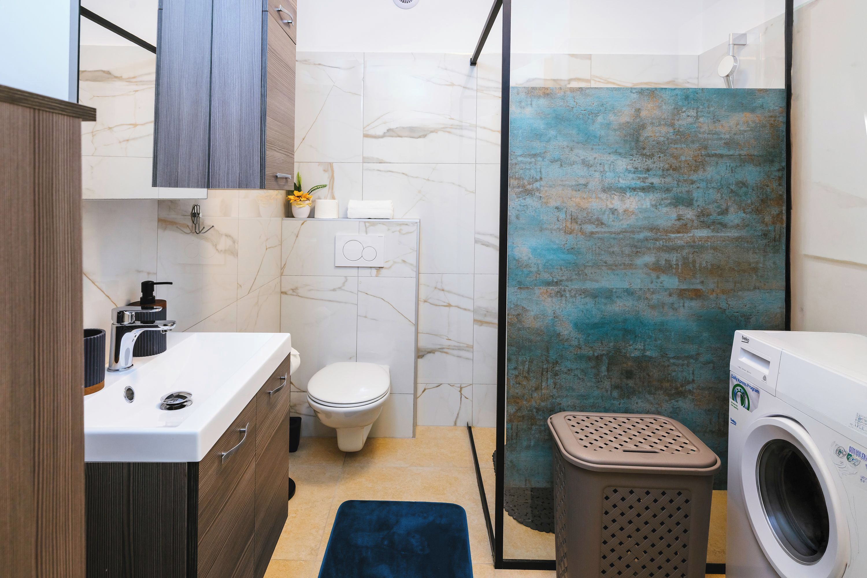 A modern bathroom with a marble sink, a toilet, a shower enclosure, and a washing machine.