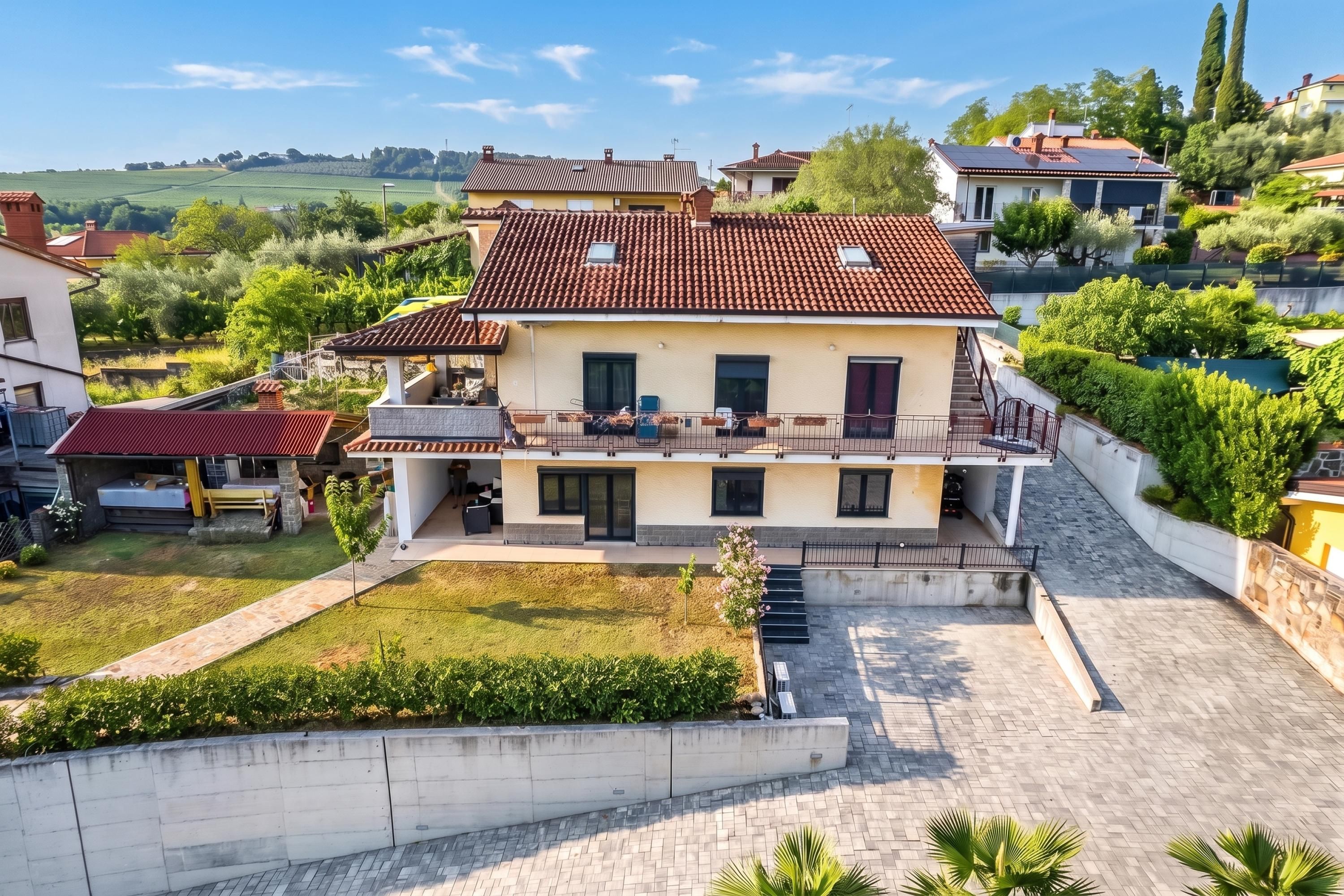 A two-story house with a tiled roof, a balcony, and a paved driveway.