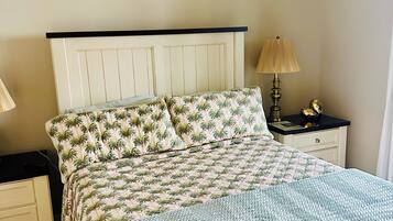 A bed with a patterned bedspread, a bedside lamp, and a nightstand with a clock.