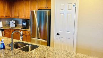 A kitchen with granite countertops, stainless steel appliances, wooden cabinets, and a white door.