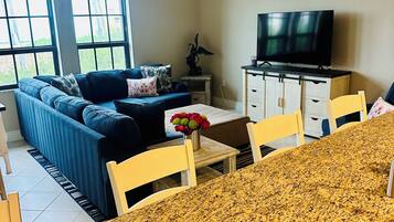 A living room with a sofa, TV, dining table, and a ceiling fan.