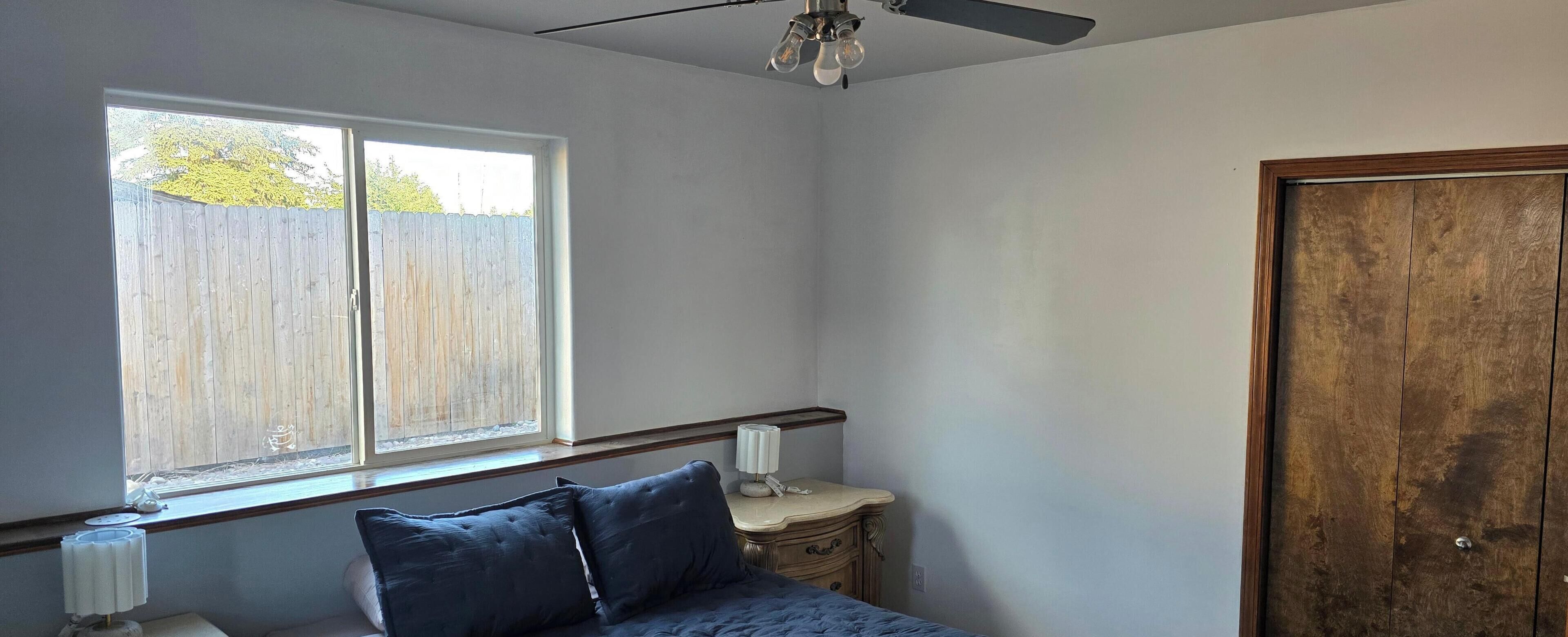 A bedroom with a bed, a nightstand, a lamp, a window, and a door.