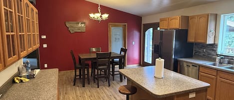 A kitchen with wooden cabinets, a granite countertop, a dining table with chairs, and a chandelier.