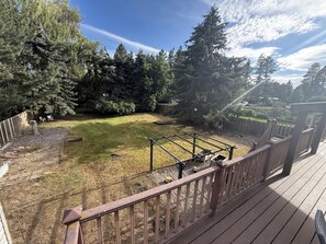 Un jardin avec une terrasse en bois, une structure de jeu en métal et divers arbres.