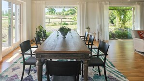 Un comedor con una mesa de madera larga, sillas negras y vista a un jardín a través de ventanas amplias.