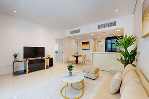 A modern living room with a TV, sofa, coffee table, and dining area. - Cozy 1 Bedroom l Burj Views from Pool Areal (Business Bay)