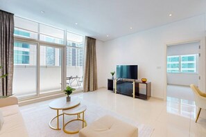A modern living room with a flat-screen TV, a sofa, a coffee table, and a dining area visible through large windows. - Cozy 1 Bedroom l Burj Views from Pool Areal (Business Bay)