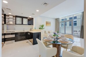 A modern kitchen with a dining area, large windows, and a view of the outside. - Cozy 1 Bedroom l Burj Views from Pool Areal (Business Bay)