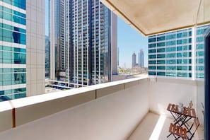 A balcony with a view of high-rise buildings, a metal chair, and a small table. - Cozy 1 Bedroom l Burj Views from Pool Areal (Business Bay)